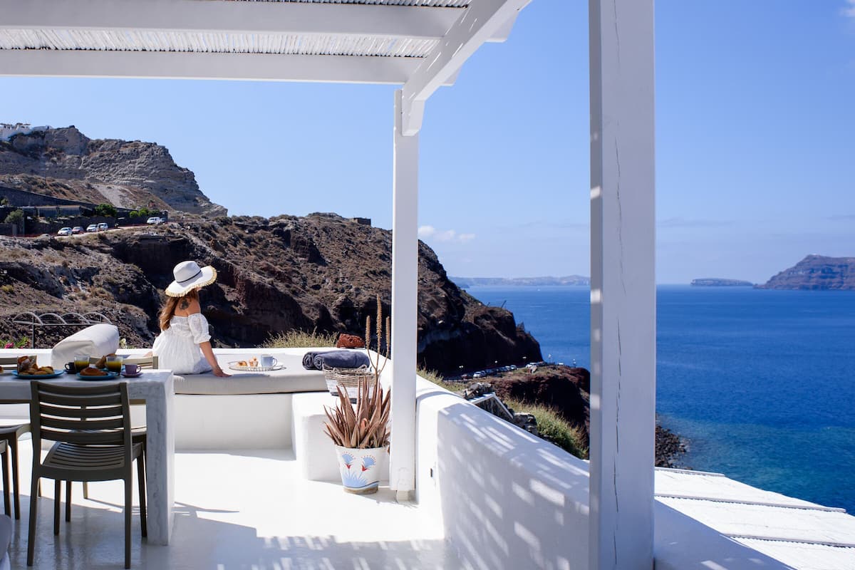 A terrace with a view of the sea, a dining table, chairs, and a person.