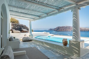 A modern outdoor pool area with a view of the sea and cliffs. - Ode Villa (Santorini)