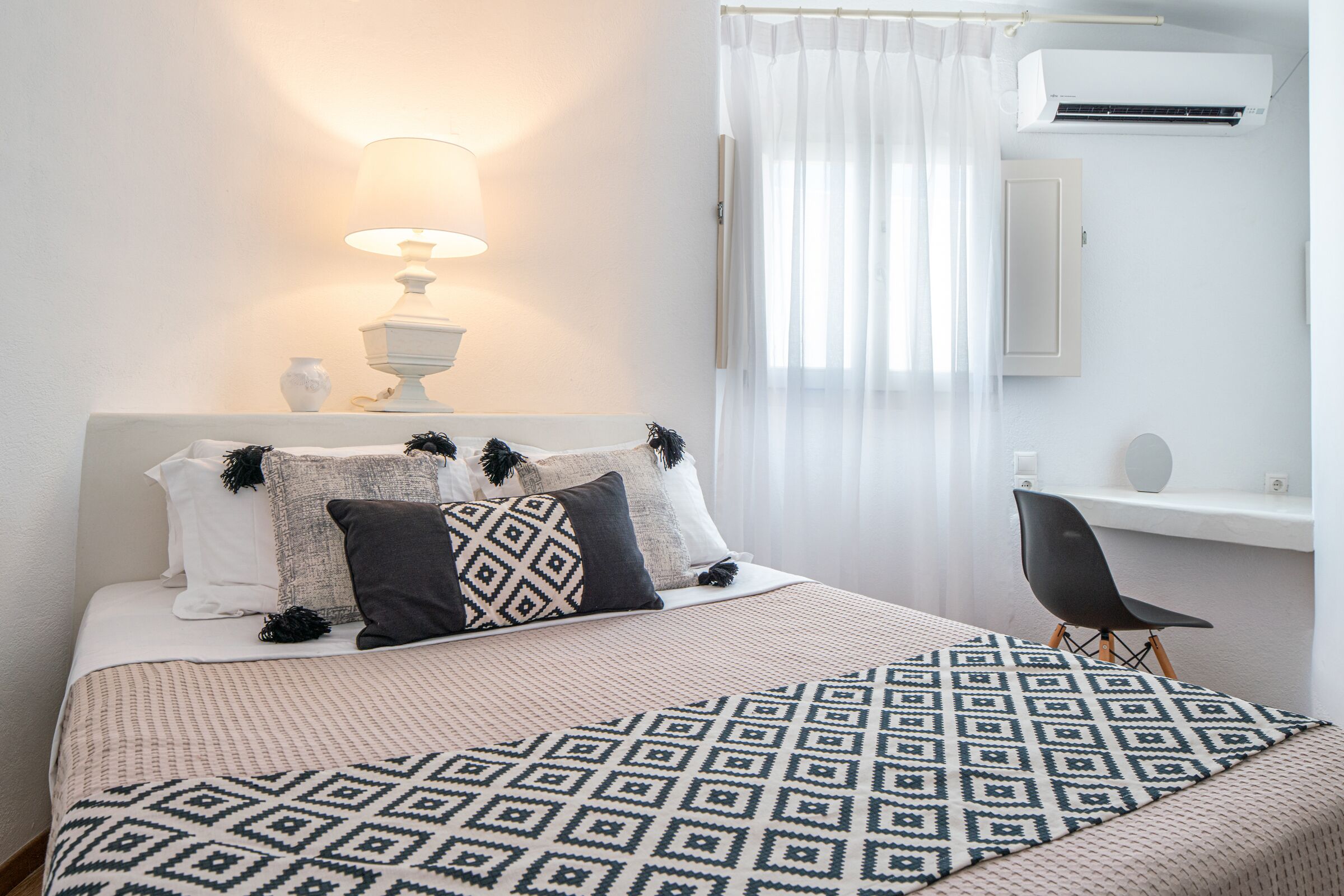Un dormitorio ordenado con cama, mesita de noche, lámpara y aire acondicionado.
