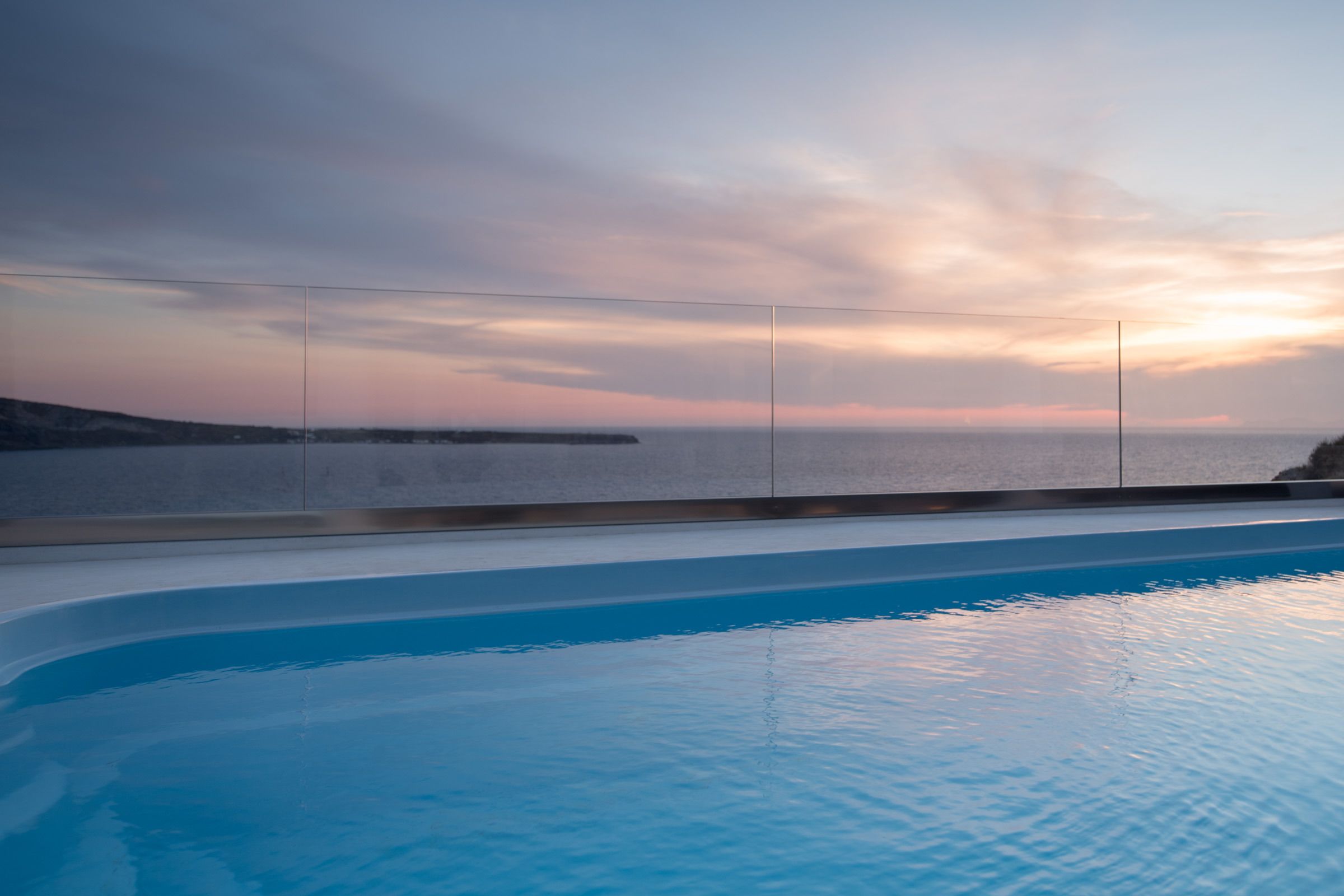 A swimming pool with a view of the sea and a sunset.