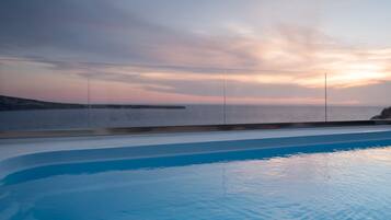 A swimming pool with a view of the sea and a sunset.