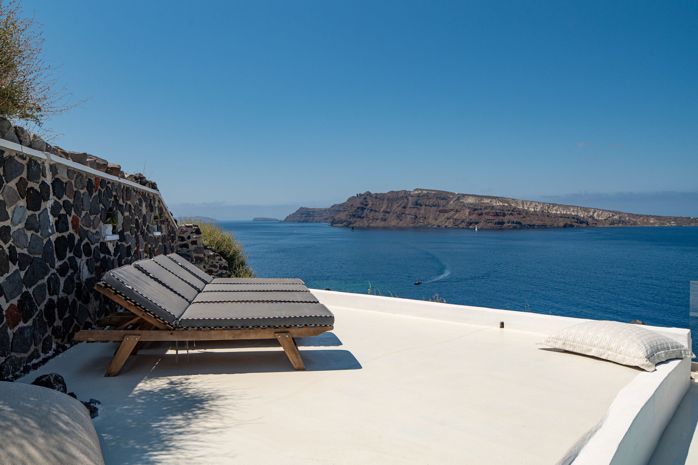 A sun lounger with a stone wall backdrop, overlooking a coastal view with cliffs and the sea.