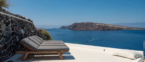 A sun lounger with a stone wall backdrop, overlooking a coastal view with cliffs and the sea.