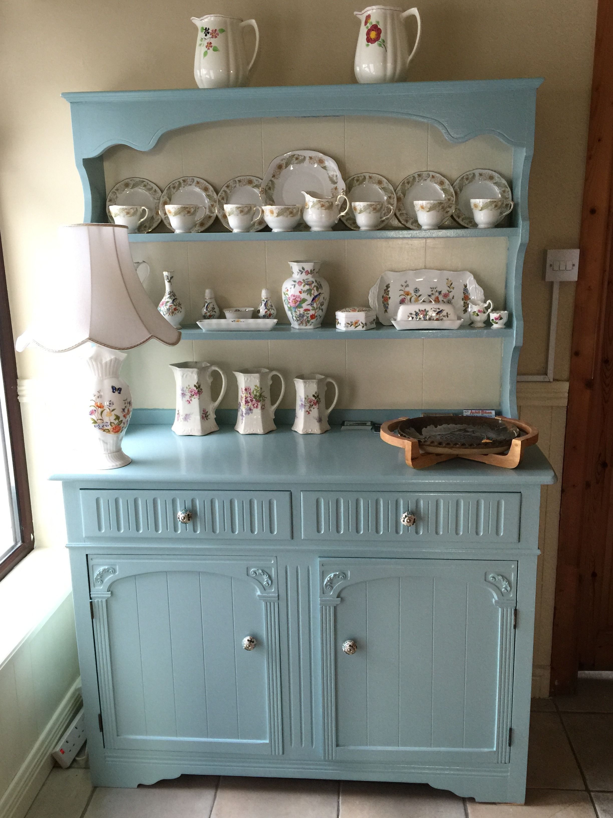 A light blue wooden cabinet with multiple shelves holding various white ceramic kitchenware items.