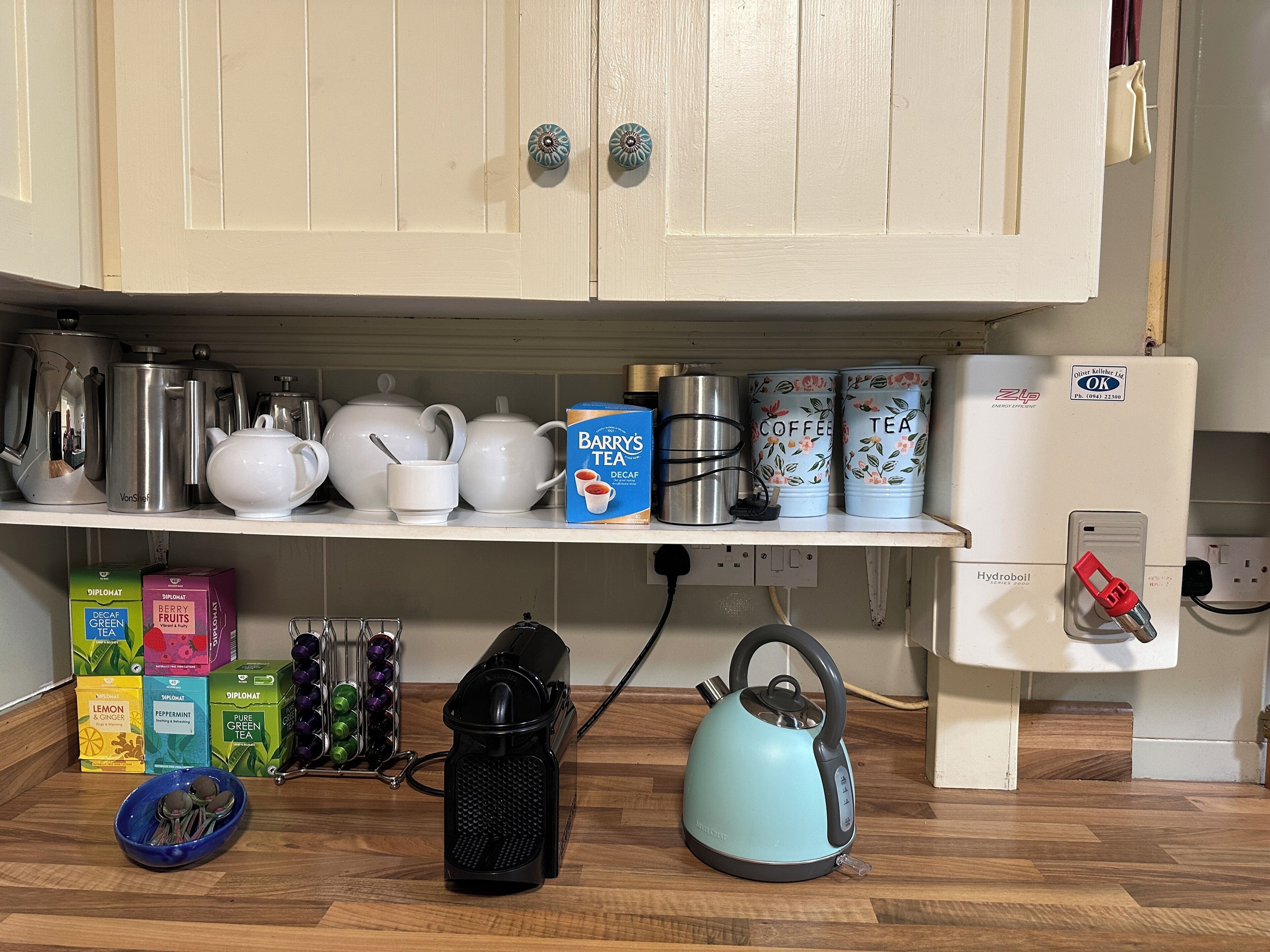 A kitchen with white cabinets, a coffee maker, tea kettles, and various tea boxes.