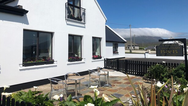 Een wit gebouw met een balkon, een naambord en een verhard buitengebied met stoelen en tafels.