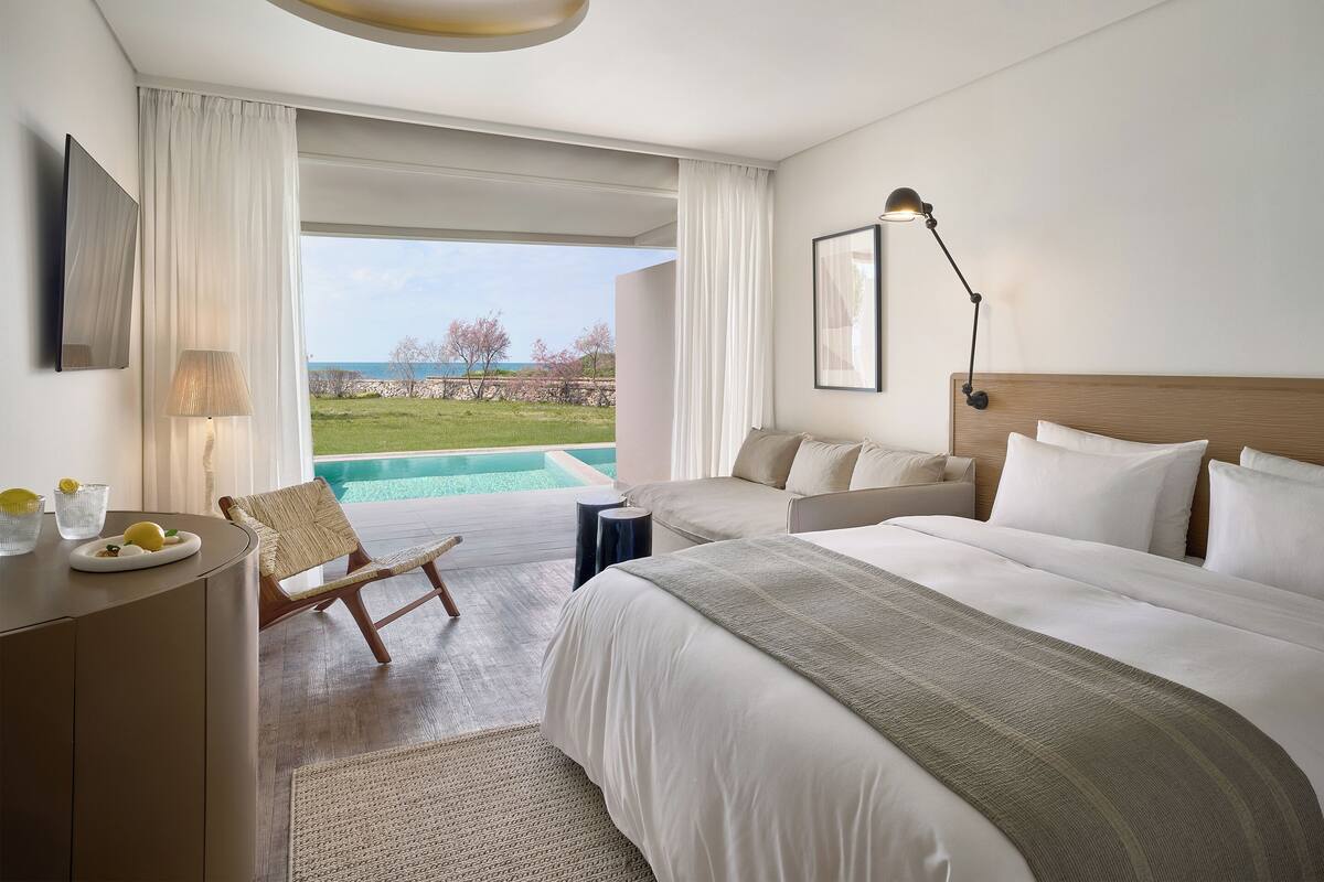 A hotel room with a large bed, a desk, a chair, a lamp, and a view of the ocean.