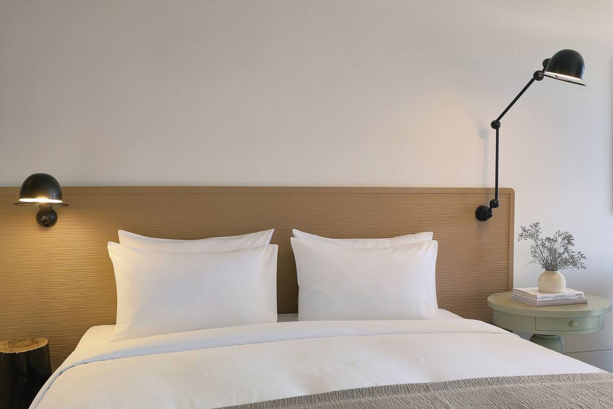 A neatly made bed with white linens and a gray throw blanket, a wooden headboard, and two wall-mounted reading lamps.
