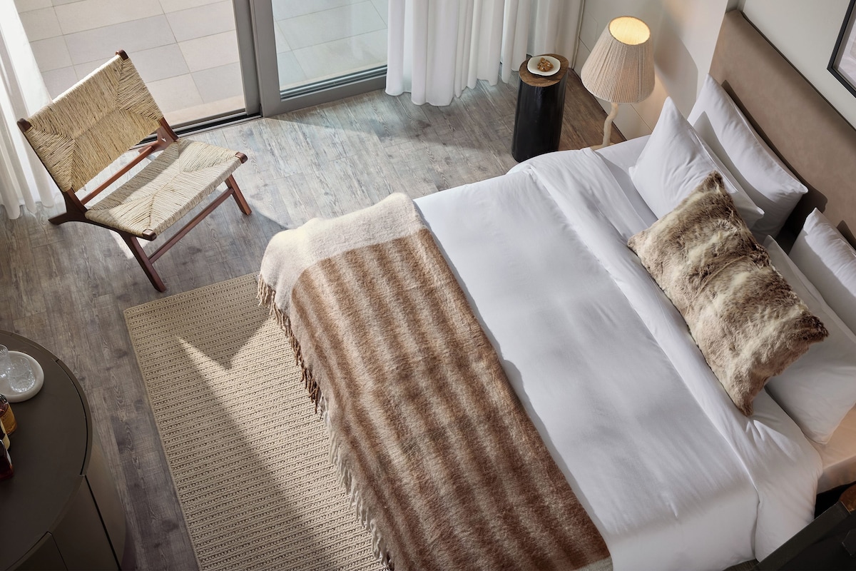 Une chambre d’hôtel avec un lit, une chaise, une lampe et une vue sur l’extérieur.