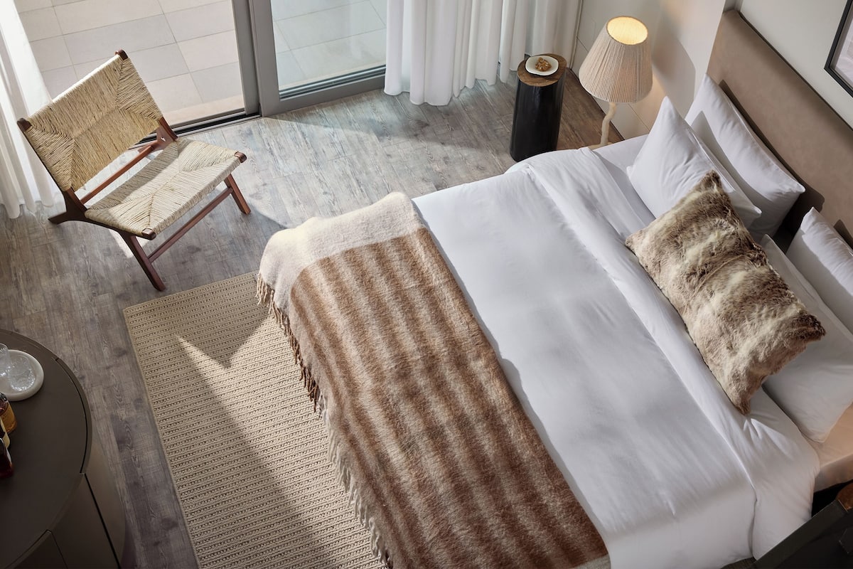 A hotel room with a bed, a chair, a lamp, and a view of the outside.