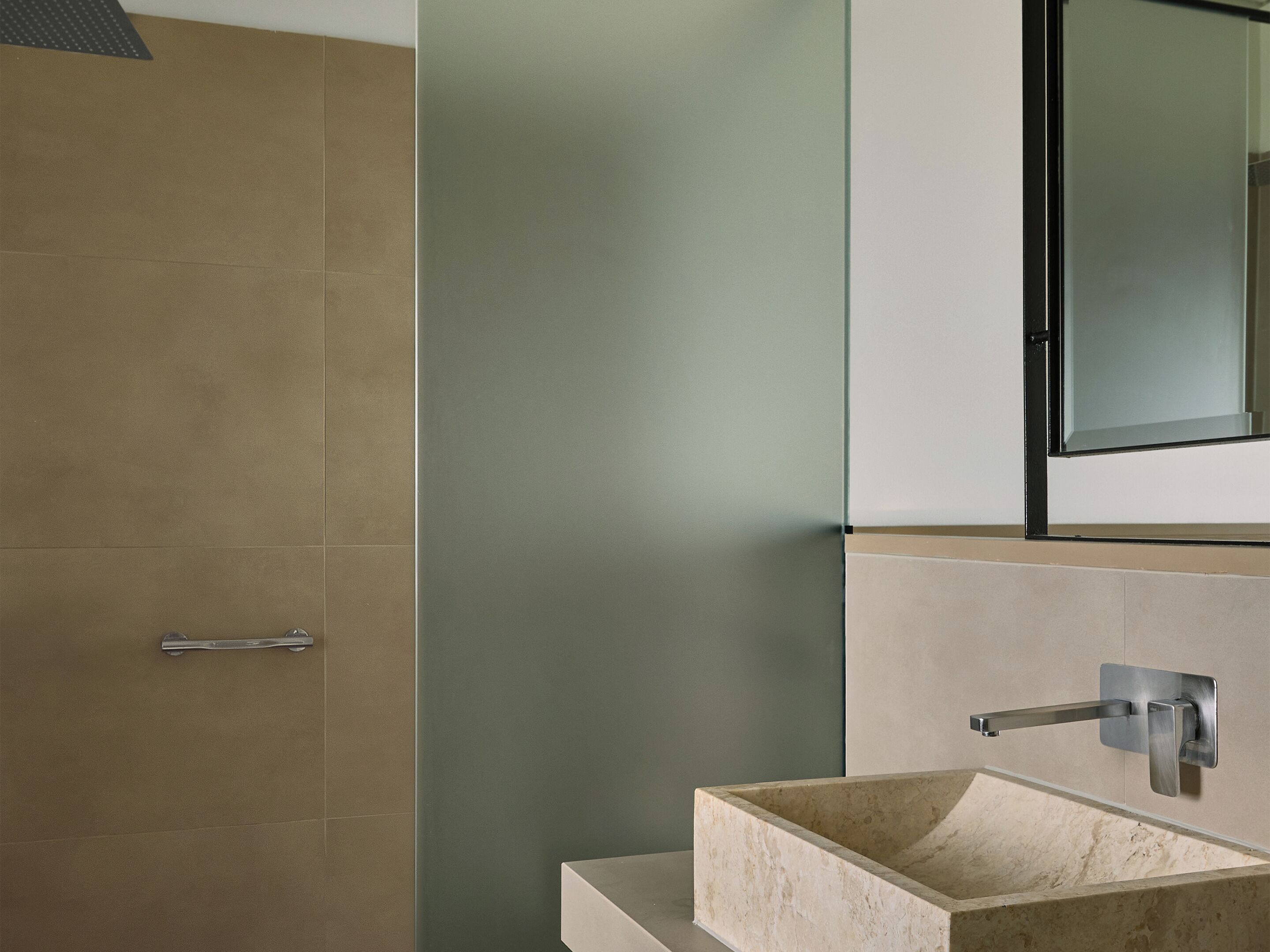 Un baño con ducha de azulejos color beige, lavamanos blanco con lavabo de mármol y un espejo sobre el lavamanos.