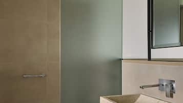 A bathroom with a beige tiled shower, a white sink with a marble basin, and a mirror above the sink.