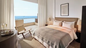 Habitación de hotel con cama, escritorio, silla, lámpara y vista al mar.