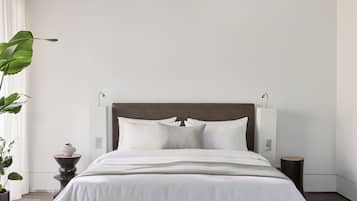 Une chambre à coucher moderne avec un grand lit, du linge de lit blanc, une tête de lit en bois, des lampes de chevet et une plante en pot.
