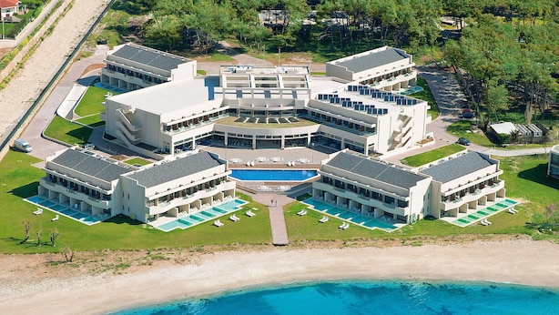 Un hotel moderno con varias construcciones, una piscina central y ubicación frente a la playa.