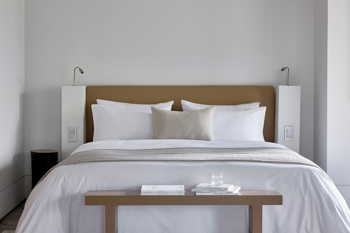 A neatly made bed with white linens, a wooden headboard, and two bedside tables with books and a glass.