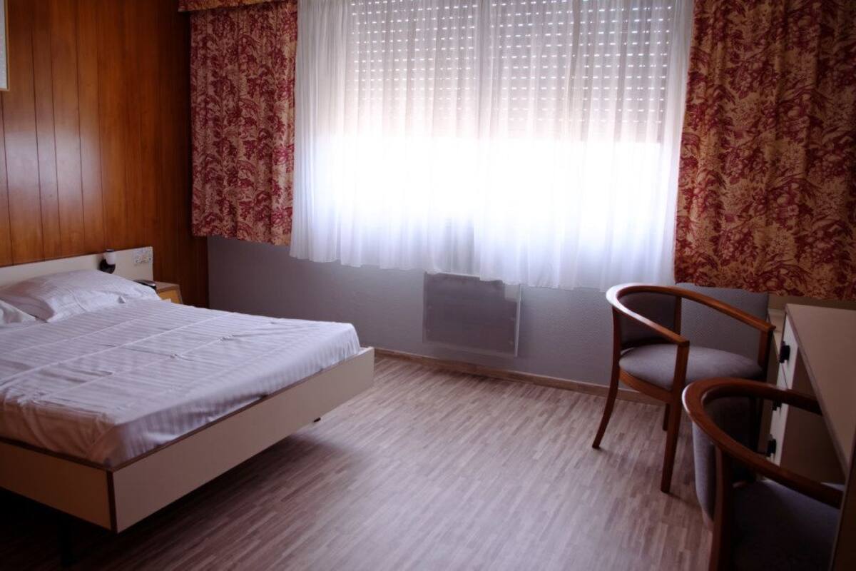 A bedroom with a bed, a chair, and a window with curtains.