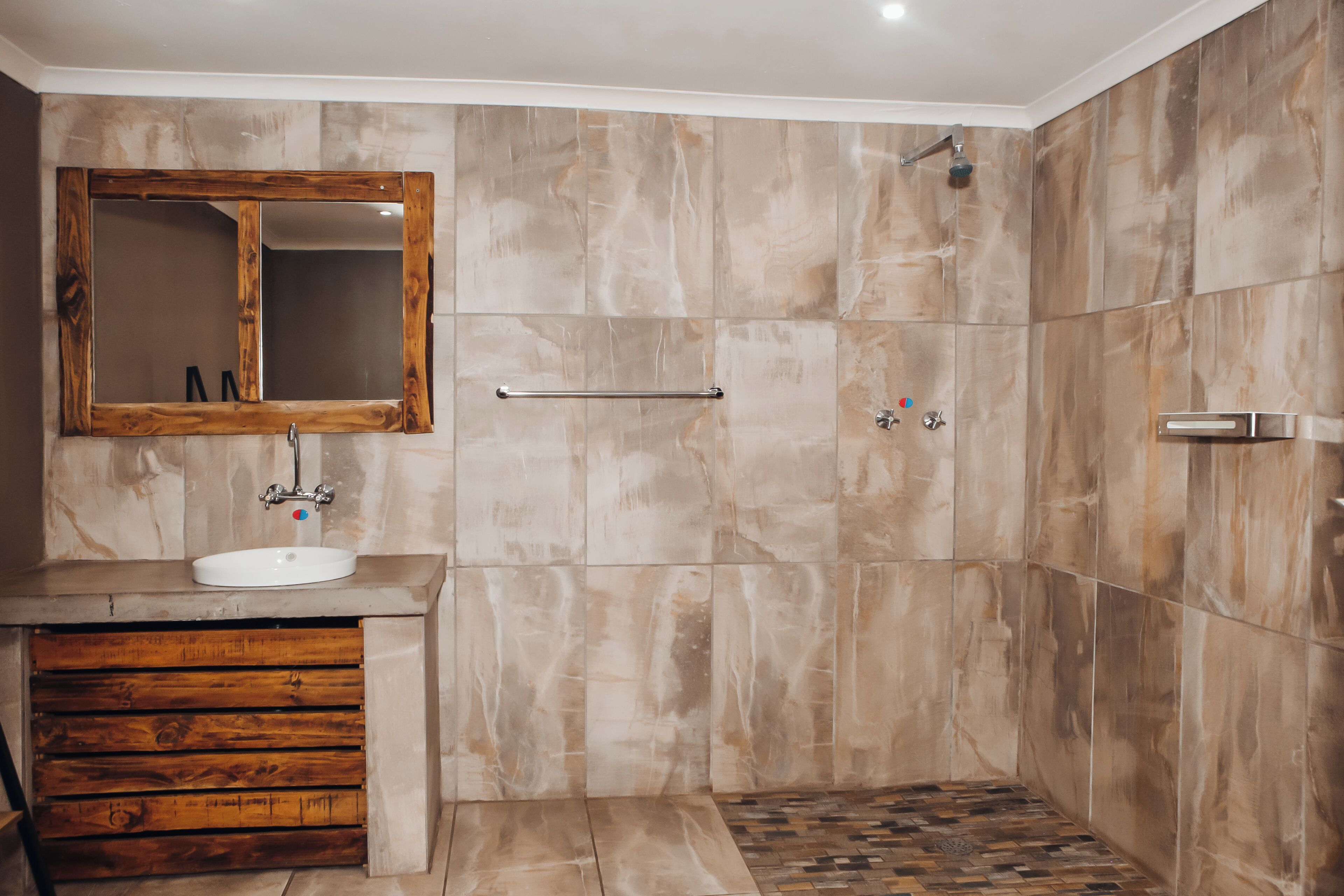 A bathroom with a wooden vanity, a large mirror, and a shower area with a tiled floor.