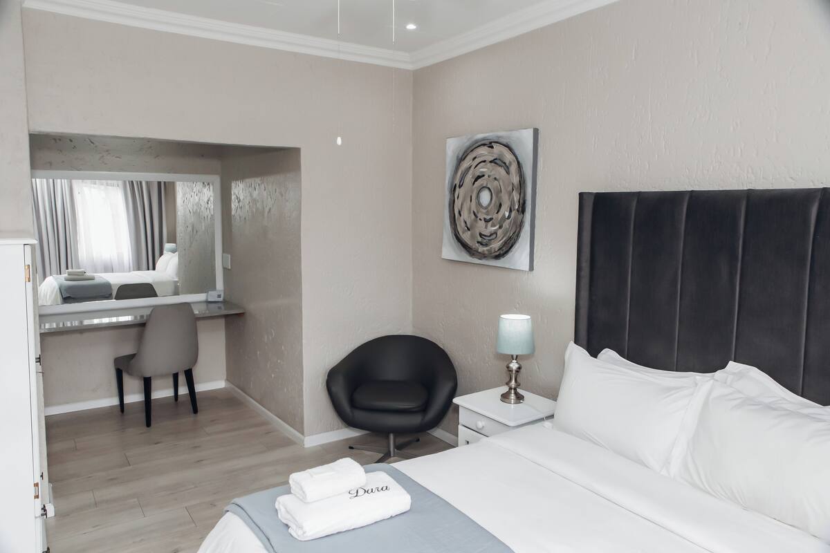 Habitación de hotel con cama, escritorio, silla, mesita de noche con lámpara y un cuadro abstracto grande en la pared.