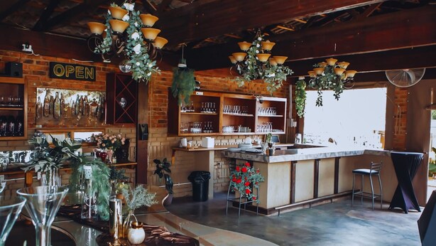 A bar area with a rustic wooden ceiling, hanging light fixtures, and a brick wall with a 'OPEN' sign. - Dara Guest House (Secunda)
