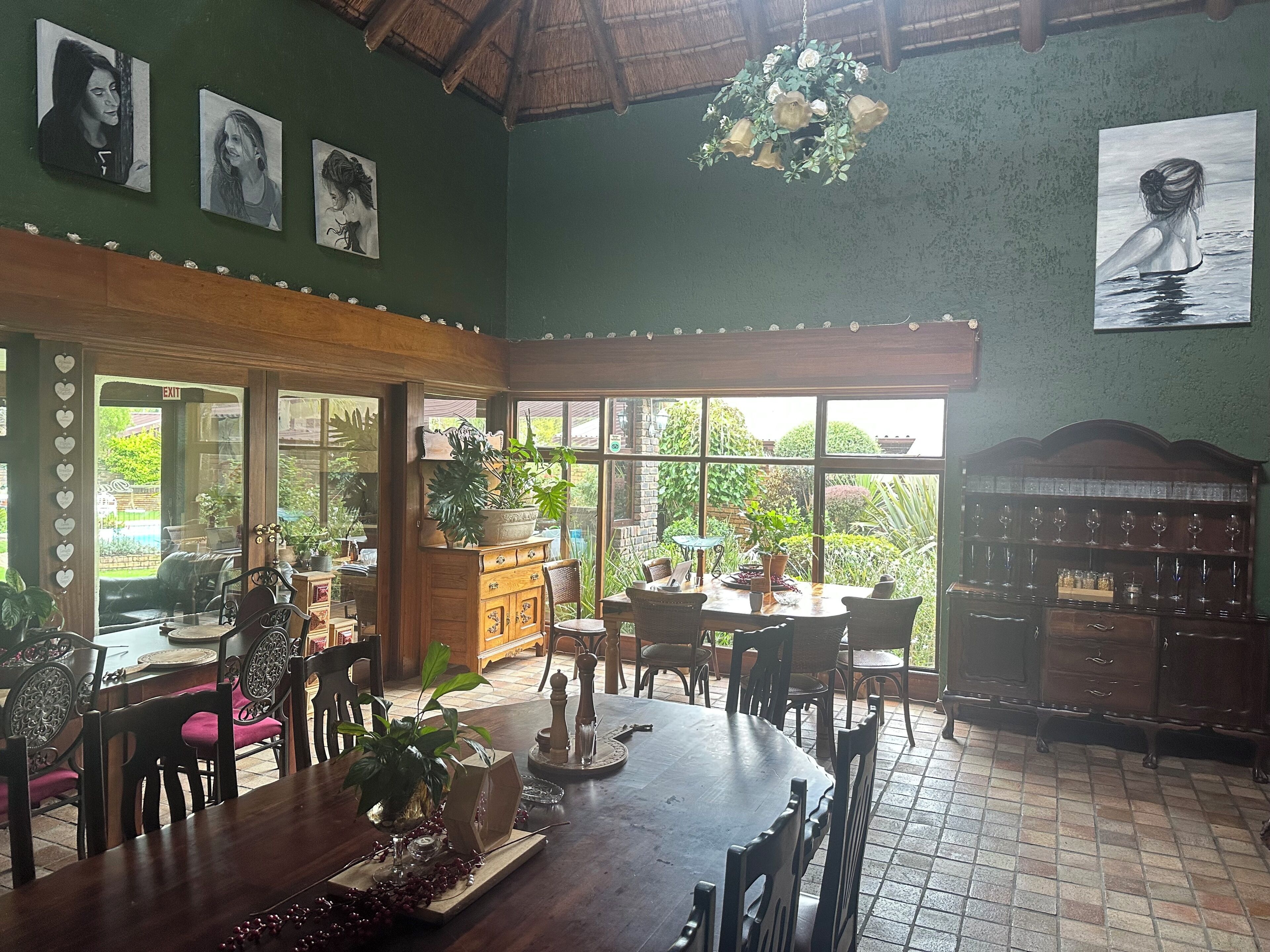 A dining area with a wooden table, chairs, a chandelier, and a view of greenery outside.