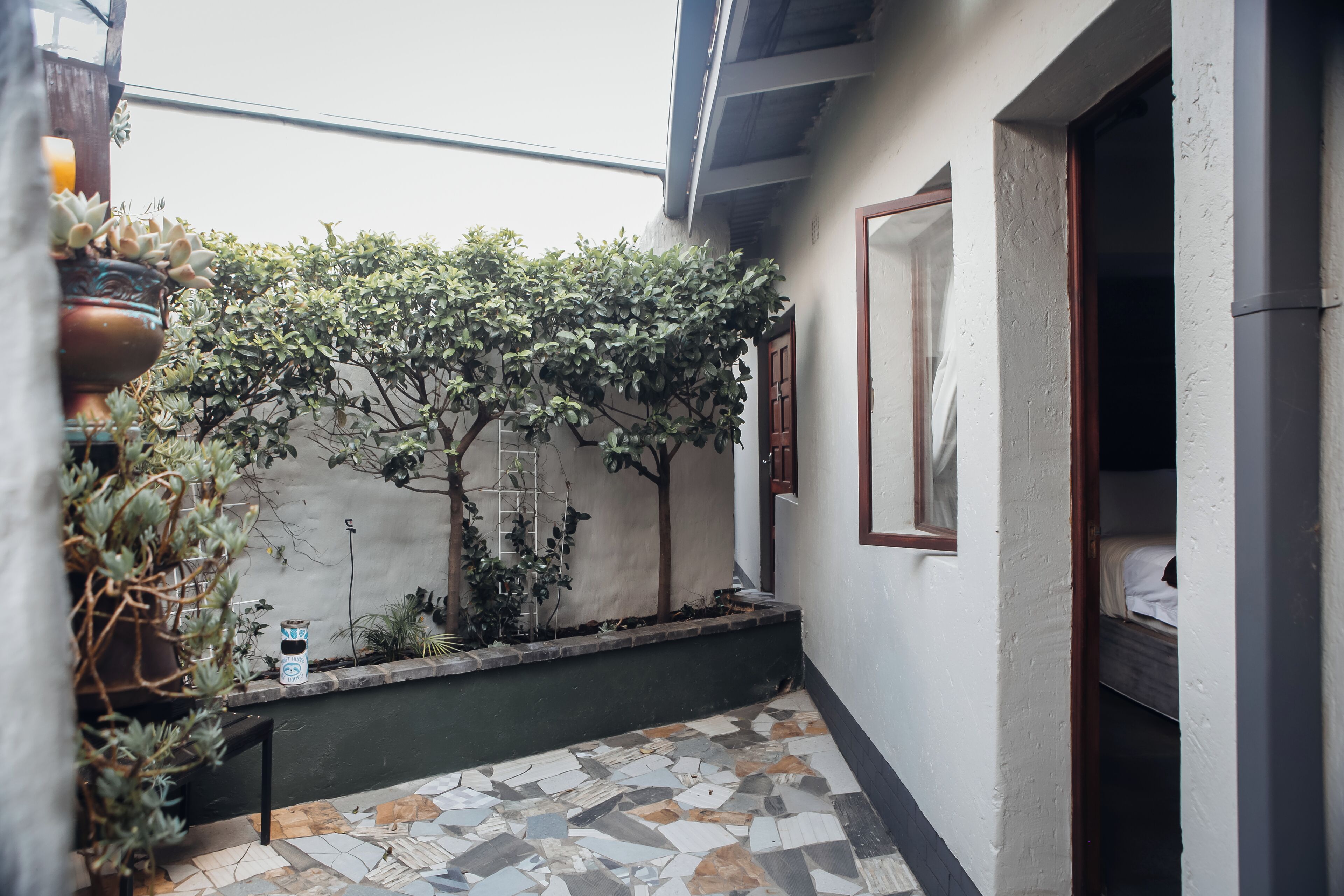 A small, enclosed outdoor area with a tiled floor, a potted plant, and a wall-mounted shelf.