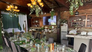 A dining area with a round table set for six, surrounded by chairs, with a brick wall and wooden ceiling in the background. - Dara Guest House (Secunda)
