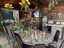 Un comedor con una mesa redonda dispuesta para seis personas, rodeada de sillas, con una pared de ladrillo y techo de madera al fondo.