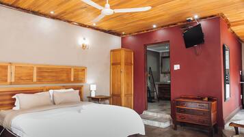 Camera da letto con un letto, testiera in legno, ventilatore a soffitto, comò di legno e televisore montato a parete.