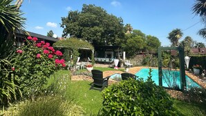 A backyard with a swimming pool, a pergola, and a garden with various plants and flowers. - Dara Guest House (Secunda)