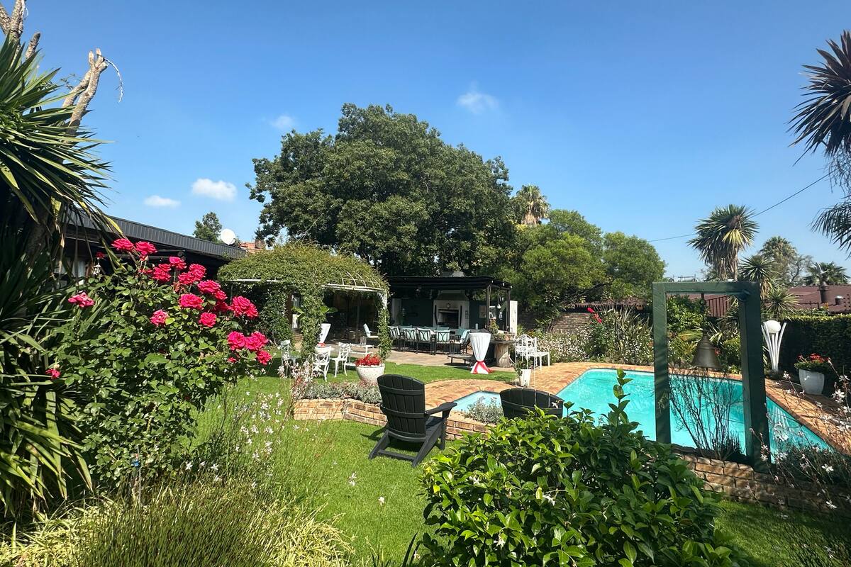 Un patio trasero con piscina, una pérgola y un jardín con diversas plantas y flores.