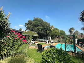Un patio trasero con piscina, una pérgola y un jardín con diversas plantas y flores.