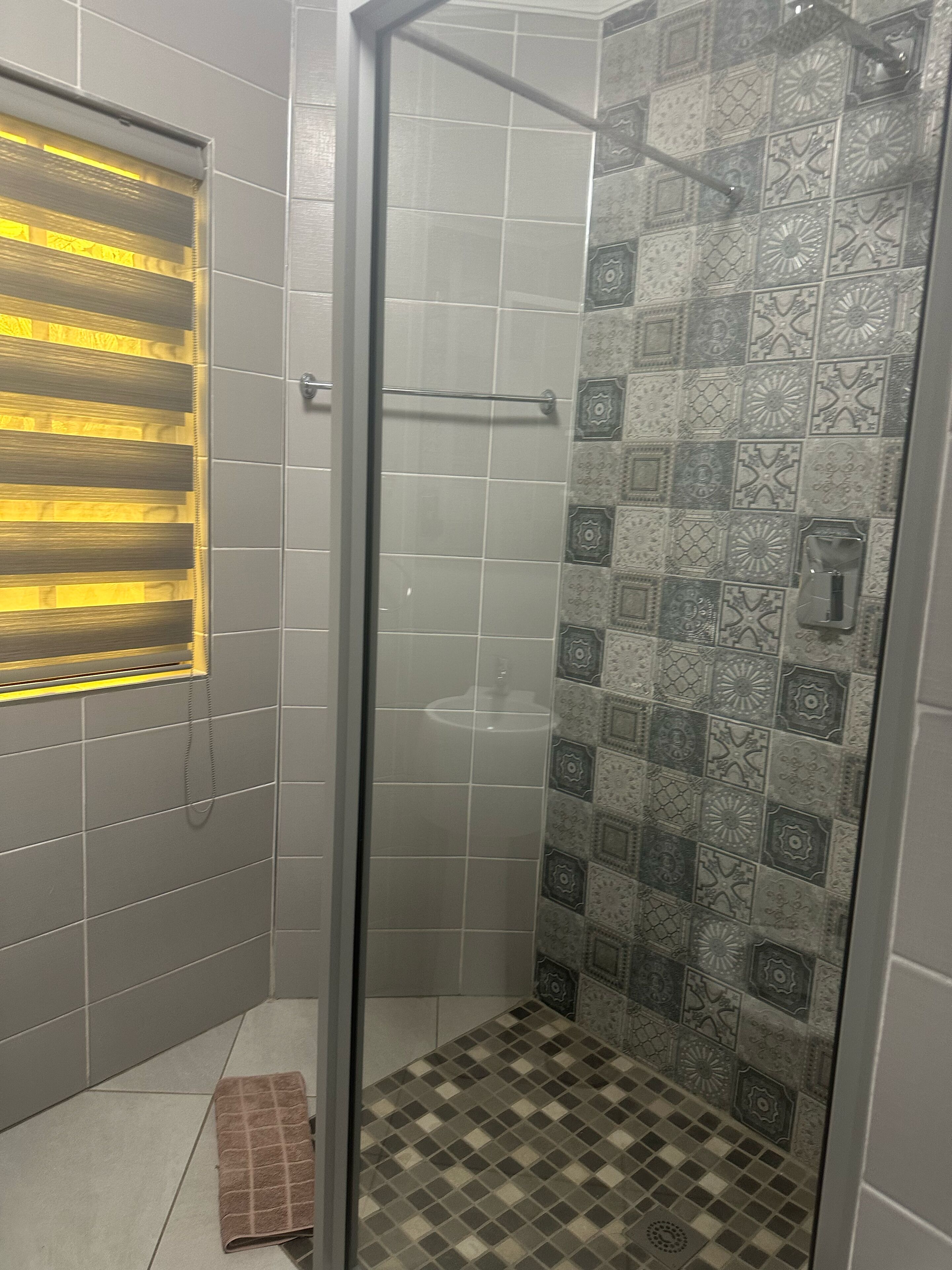 A shower with a glass door, patterned tiles, and a towel on the floor.