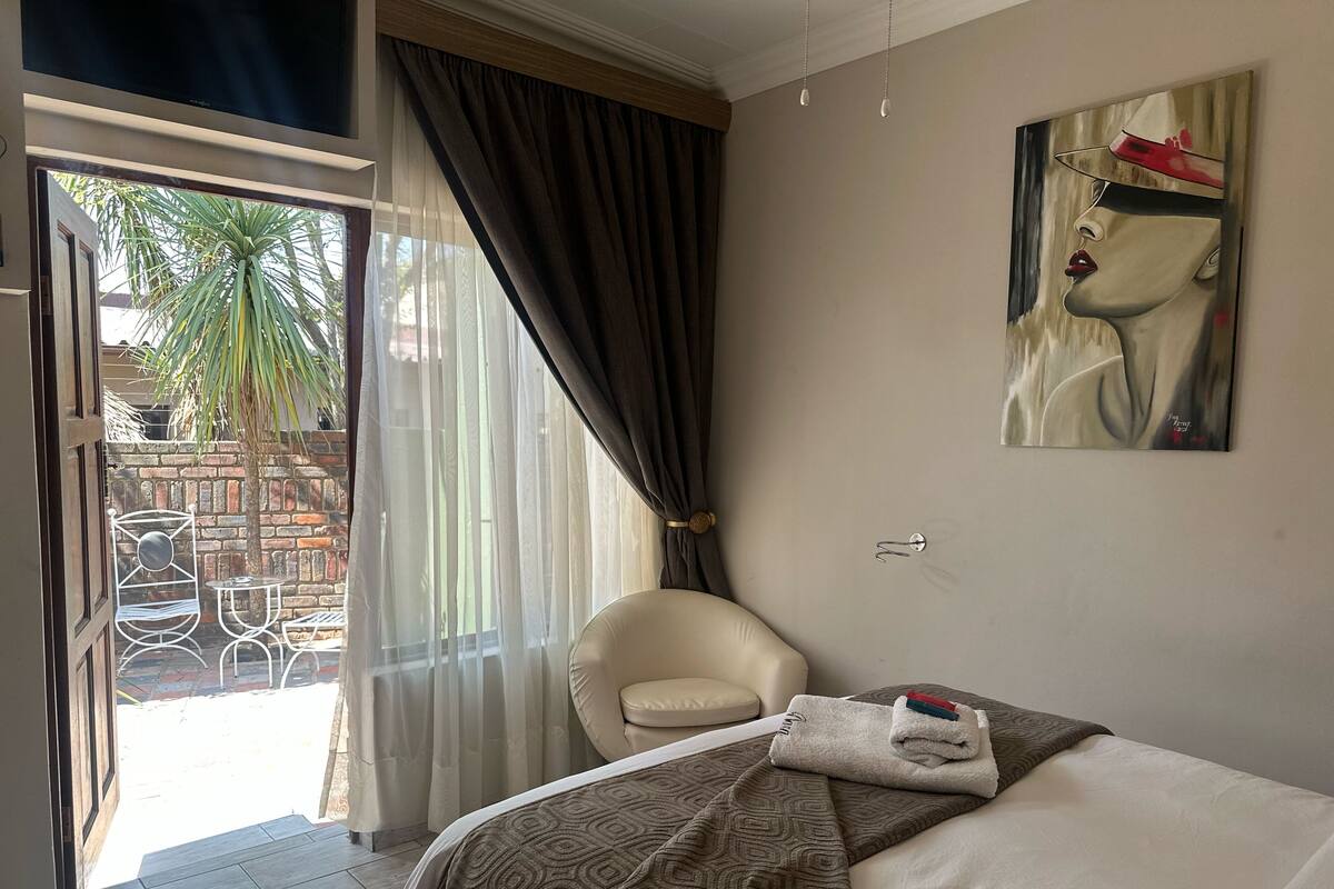 Una habitación de hotel con una cama, una silla, un cuadro y vistas al exterior.