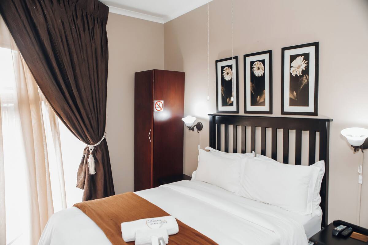 Una habitación de hotel con cama, armario de madera, mesita de noche y cuadros con motivos florales en la pared.