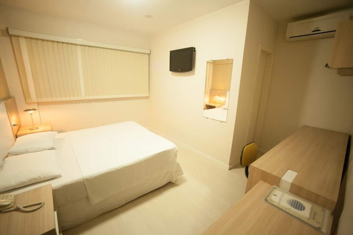 A hotel room with a bed, bedside table, lamp, mirror, and a small desk with a chair.