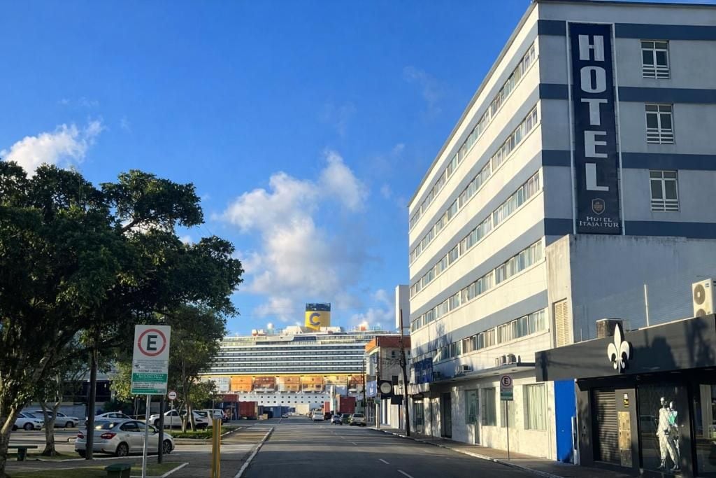 Un edificio de hotel con un letrero grande que dice 'HOTEL', un crucero grande al fondo y un cielo azul despejado.