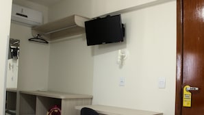 A hotel room with a bed, a desk with a chair, a television mounted on the wall, a wardrobe, and a door with a cleaning schedule sign. - Hotel Itajaí Tur (Itajai)