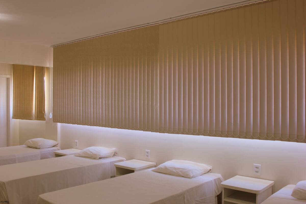 A hotel room with three single beds, each with a pillow and a nightstand.