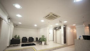 A reception area with a reception desk, several chairs, potted plants, and a staircase leading to an elevator. - Hotel Itajaí Tur (Itajai)
