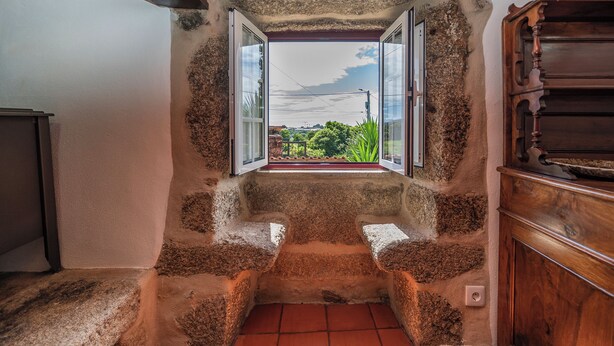 Una habitación con un banco de piedra, un armario de madera y un ventanal con vistas a la vegetación.