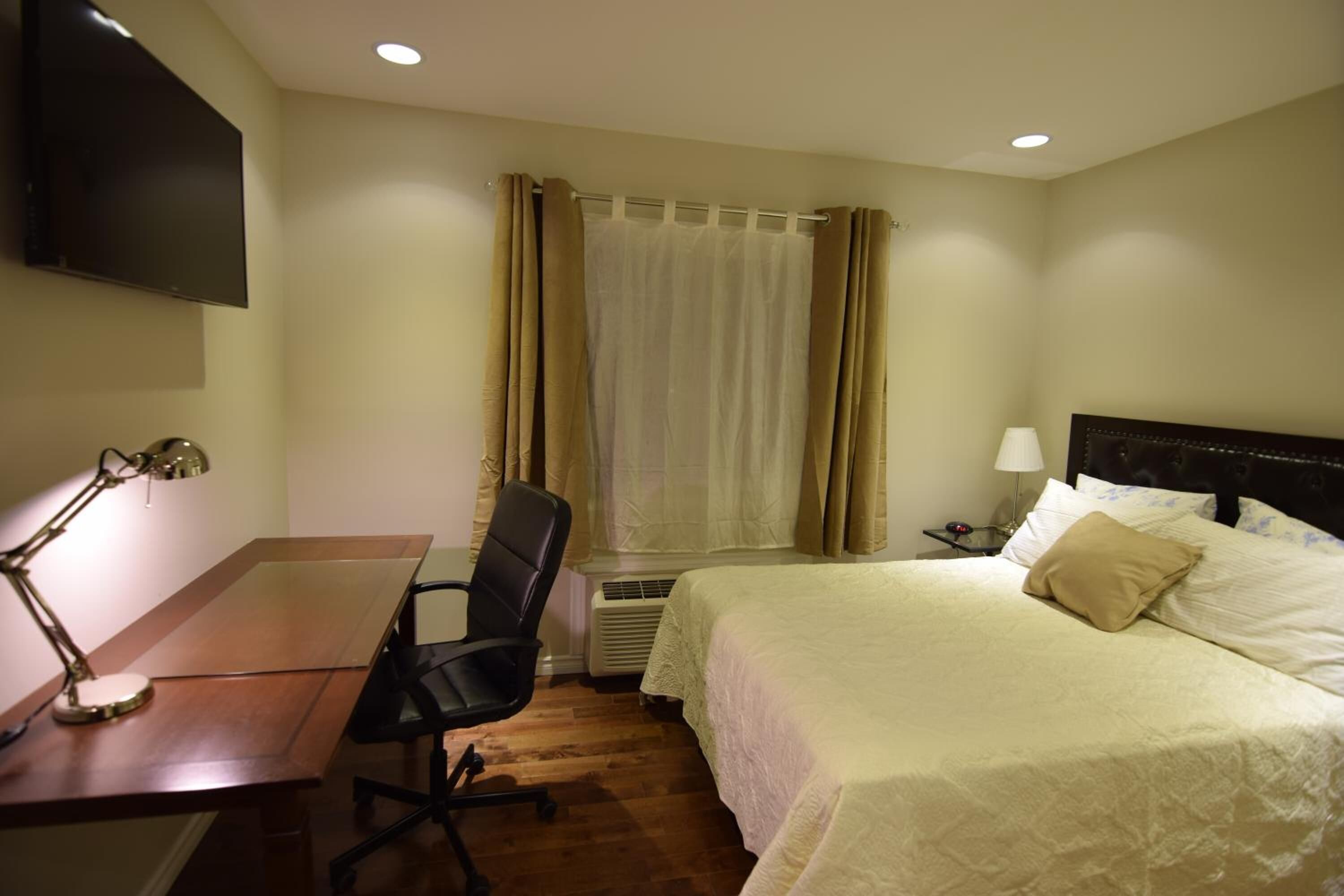 Une chambre d’hôtel comprenant un lit, un bureau avec une chaise, un téléviseur fixé au mur et une fenêtre avec des rideaux.