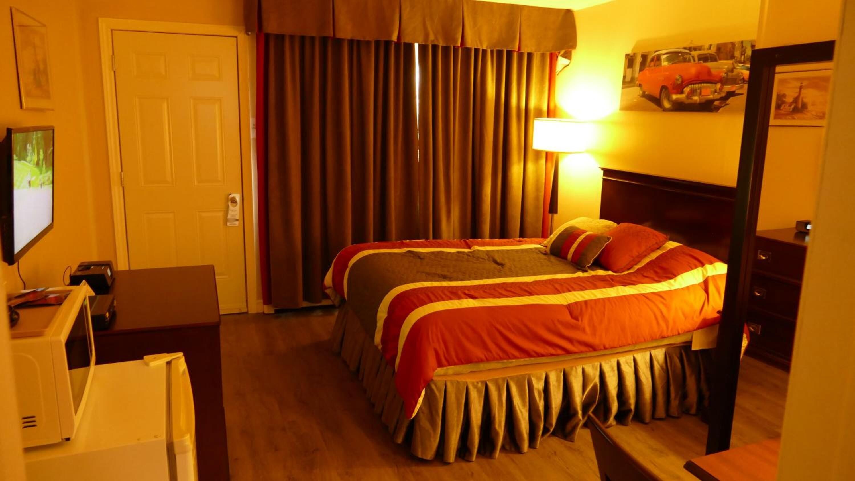 A hotel room with a bed, a desk, a lamp, and curtains.