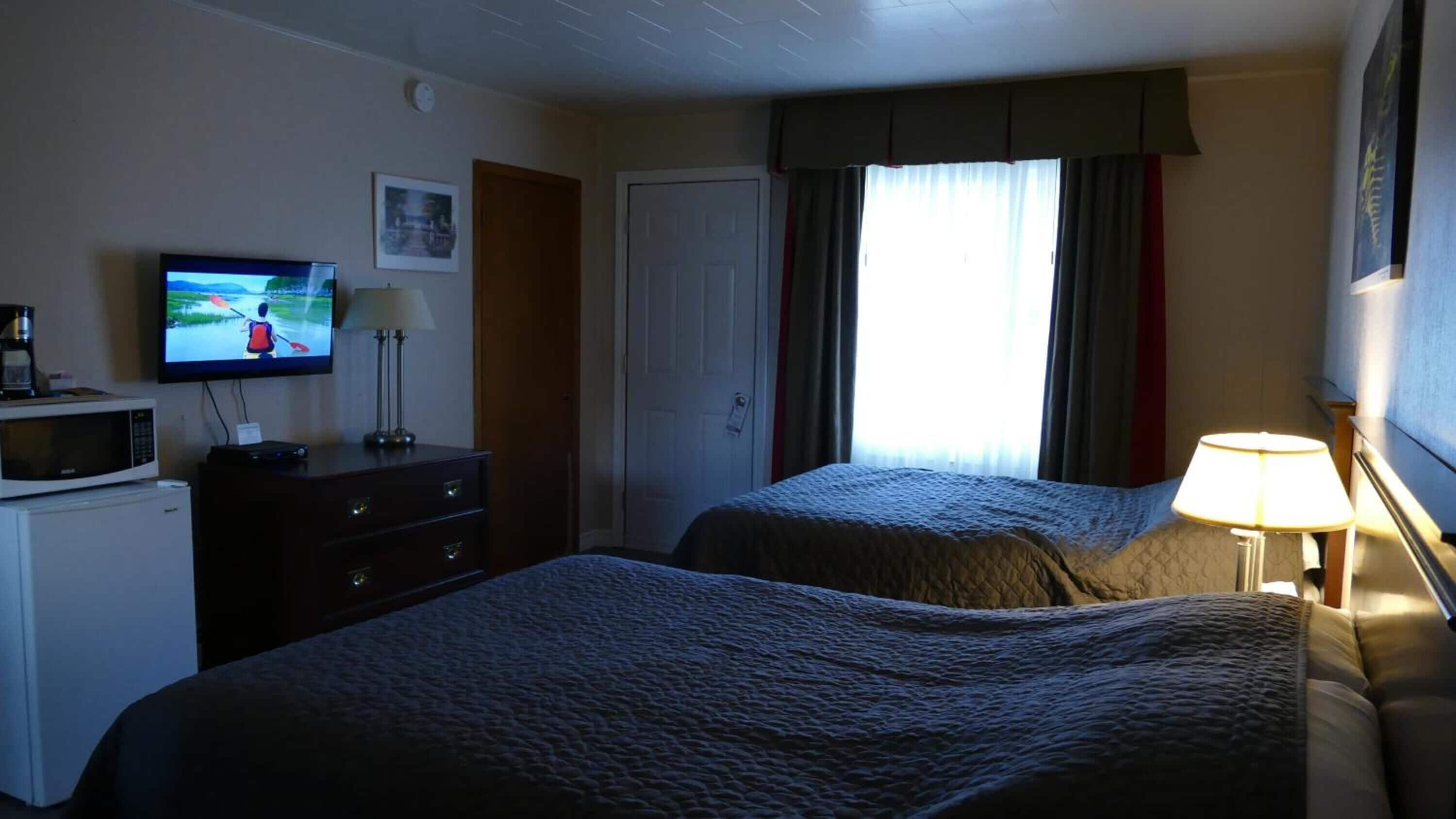 A hotel room with two beds, a television, a desk with a microwave, and a window with curtains.