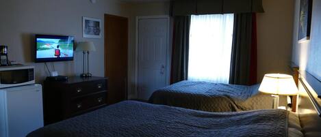 Une chambre d’hôtel avec deux lits, une télévision, un bureau avec un micro-ondes et une fenêtre avec des rideaux.