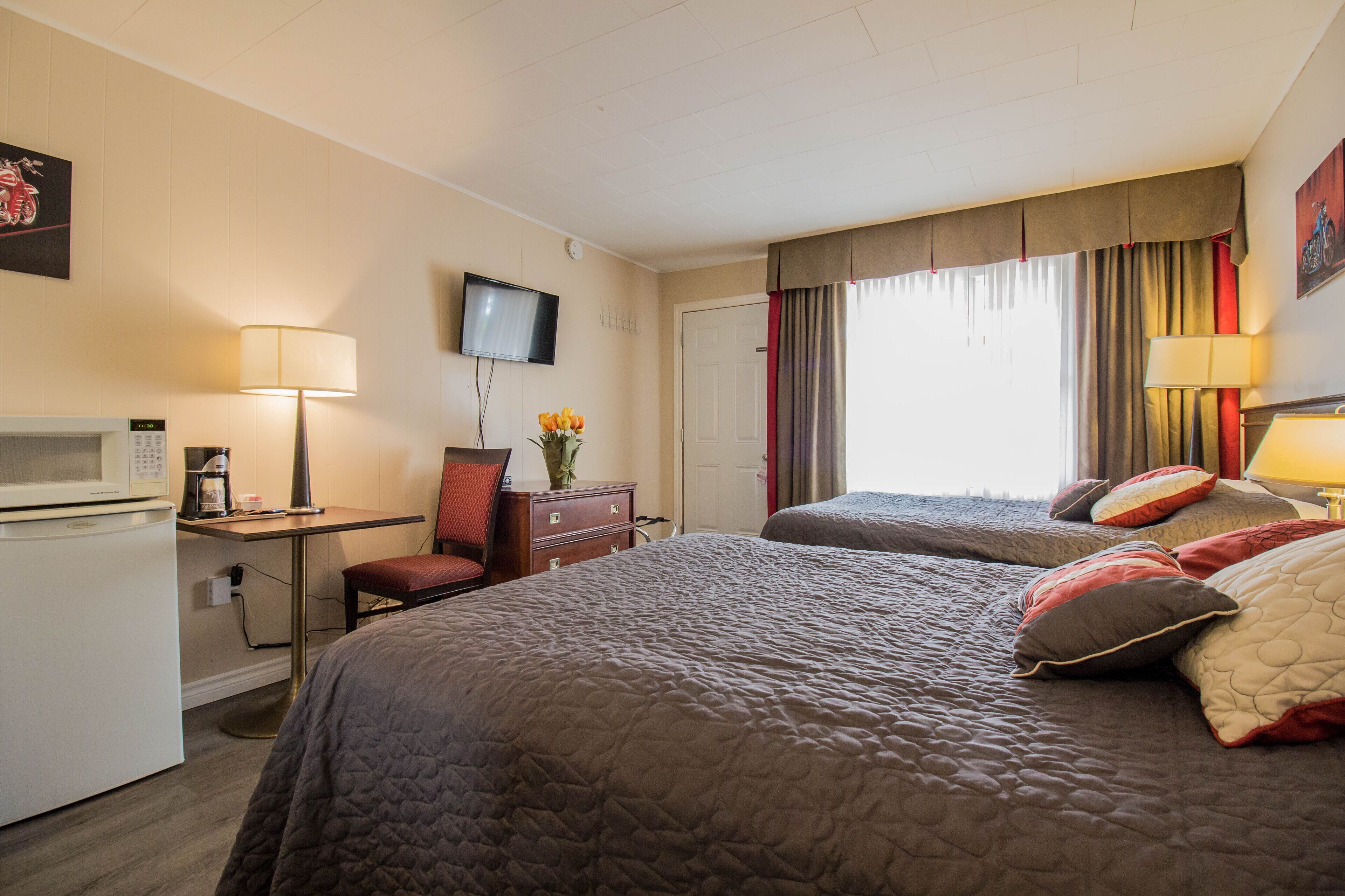 A hotel room with two beds, a desk with a computer, a microwave, and a TV.