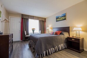 A hotel room with a large bed, two bedside tables with lamps, a dresser, a chair, a desk, and a window with curtains. - The White Horse Motel (Cornwall)