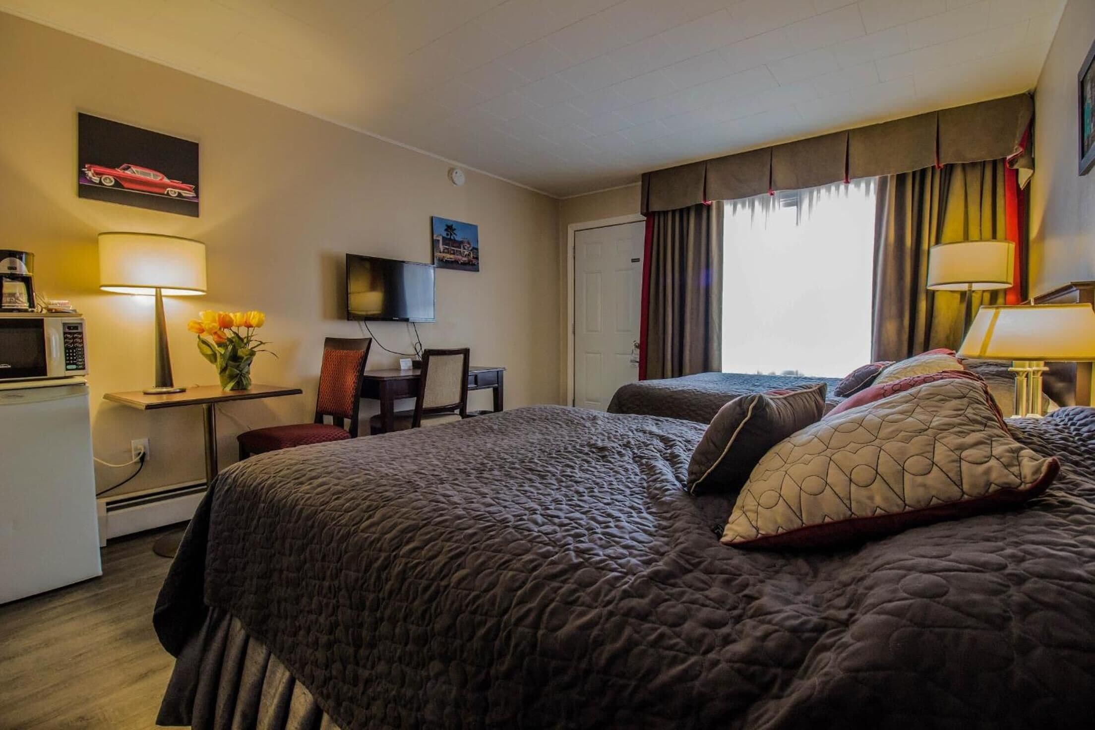 A hotel room with a large bed, a desk with a lamp, a television, and a window with curtains.