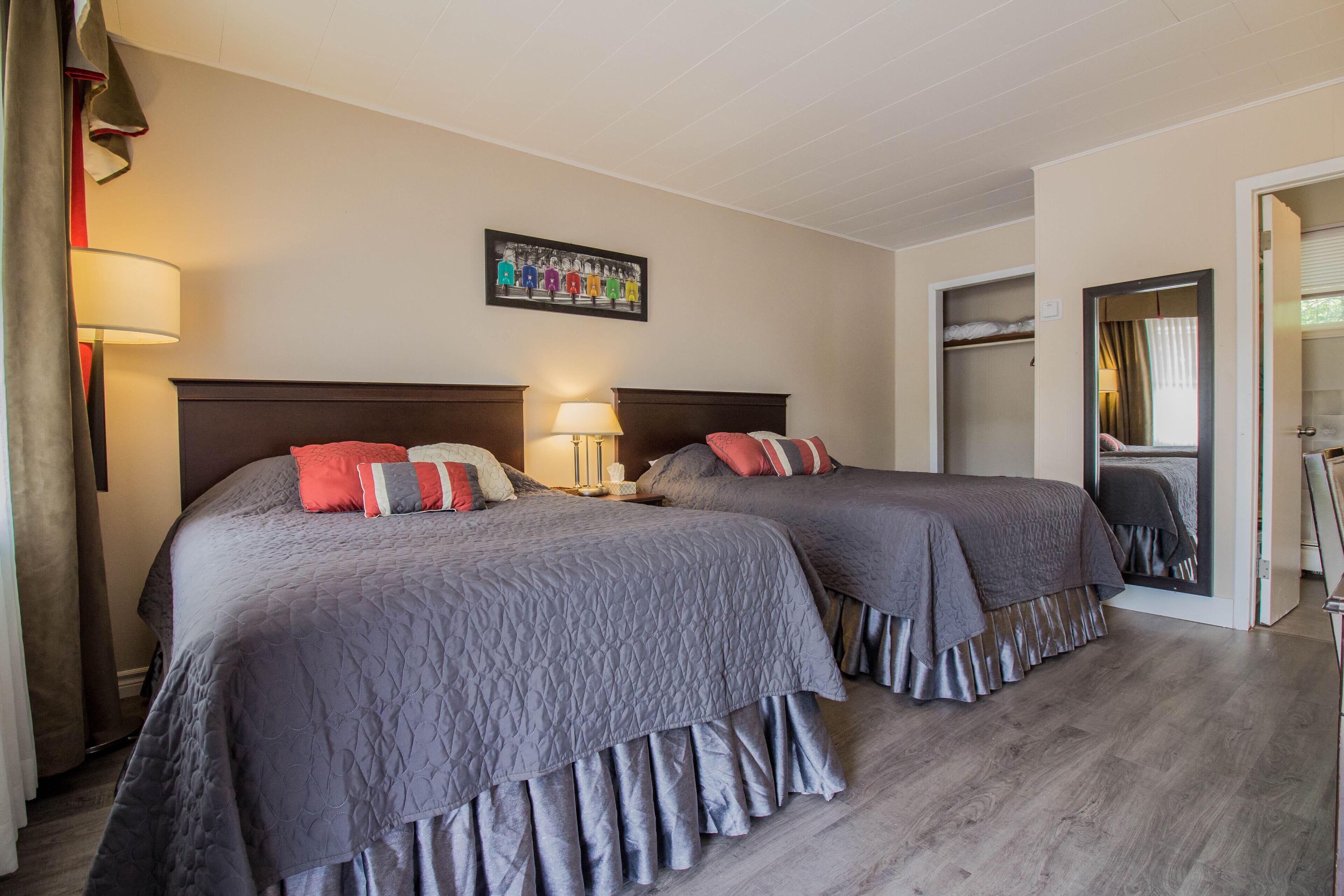 A hotel room with two beds, a mirror, a wardrobe, and a framed picture on the wall.