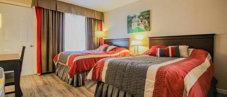 A hotel room with two beds, a desk, and a chair.